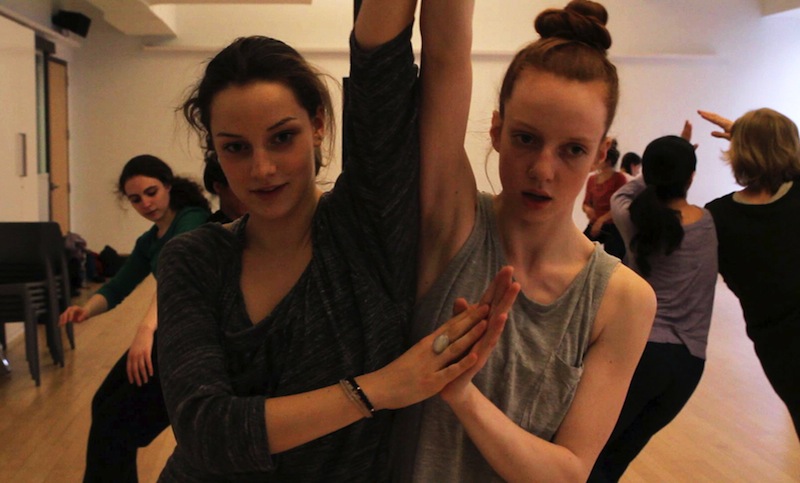 Two women lean in to one another, their hands come together in a prayer position